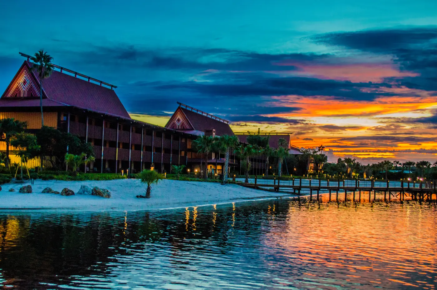 Disney's Polynesian Village Resort's thatched-look longhouses on the beach at Seven Seas Lagoon at sunset, with a long dock stretching into the water