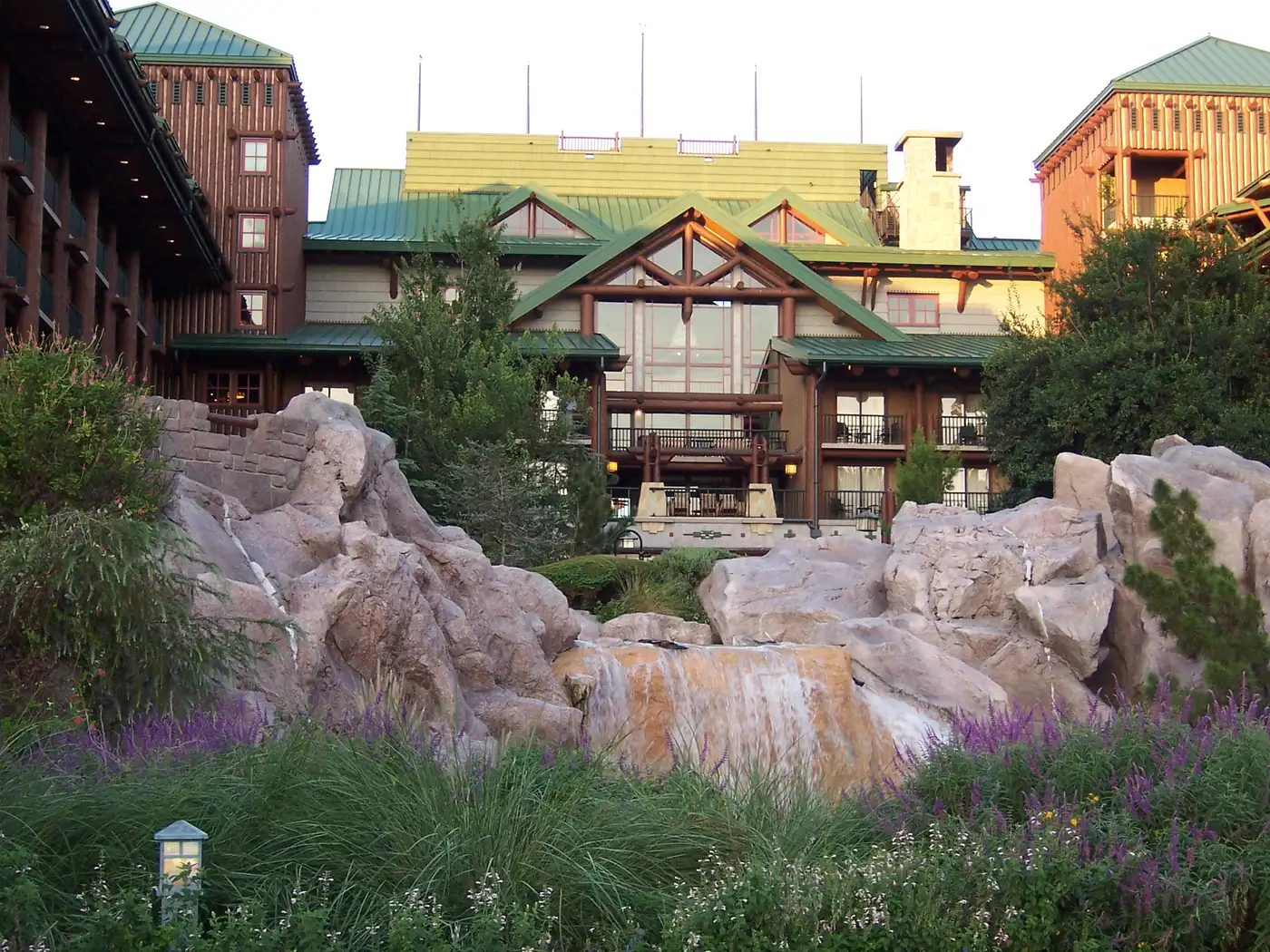 Disney's Wilderness Lodge, a rustic timber-and-stone lodge building with a green metal roof, behind a rock-and-waterfall feature