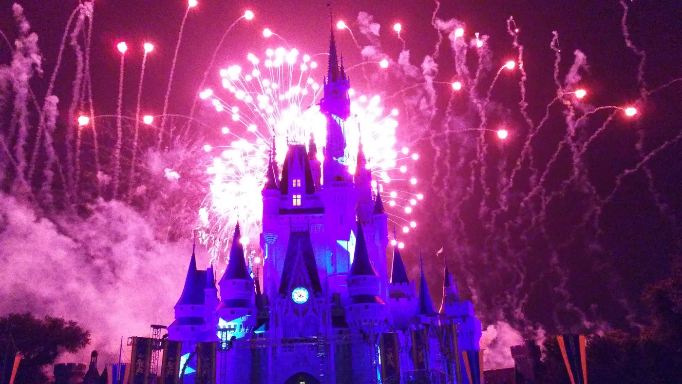 Fireworks bursting in pink and white above Cinderella Castle at Magic Kingdom at night