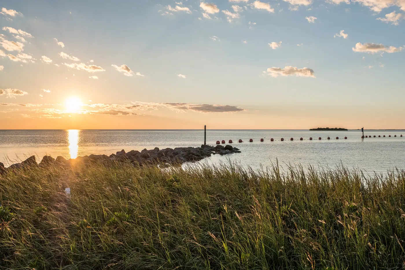 Sunset over the Gulf of Mexico at Fort Island Gulf Beach, where the Crystal River reaches open water, with a stone jetty, a line of marker buoys, and grass flats in the foreground