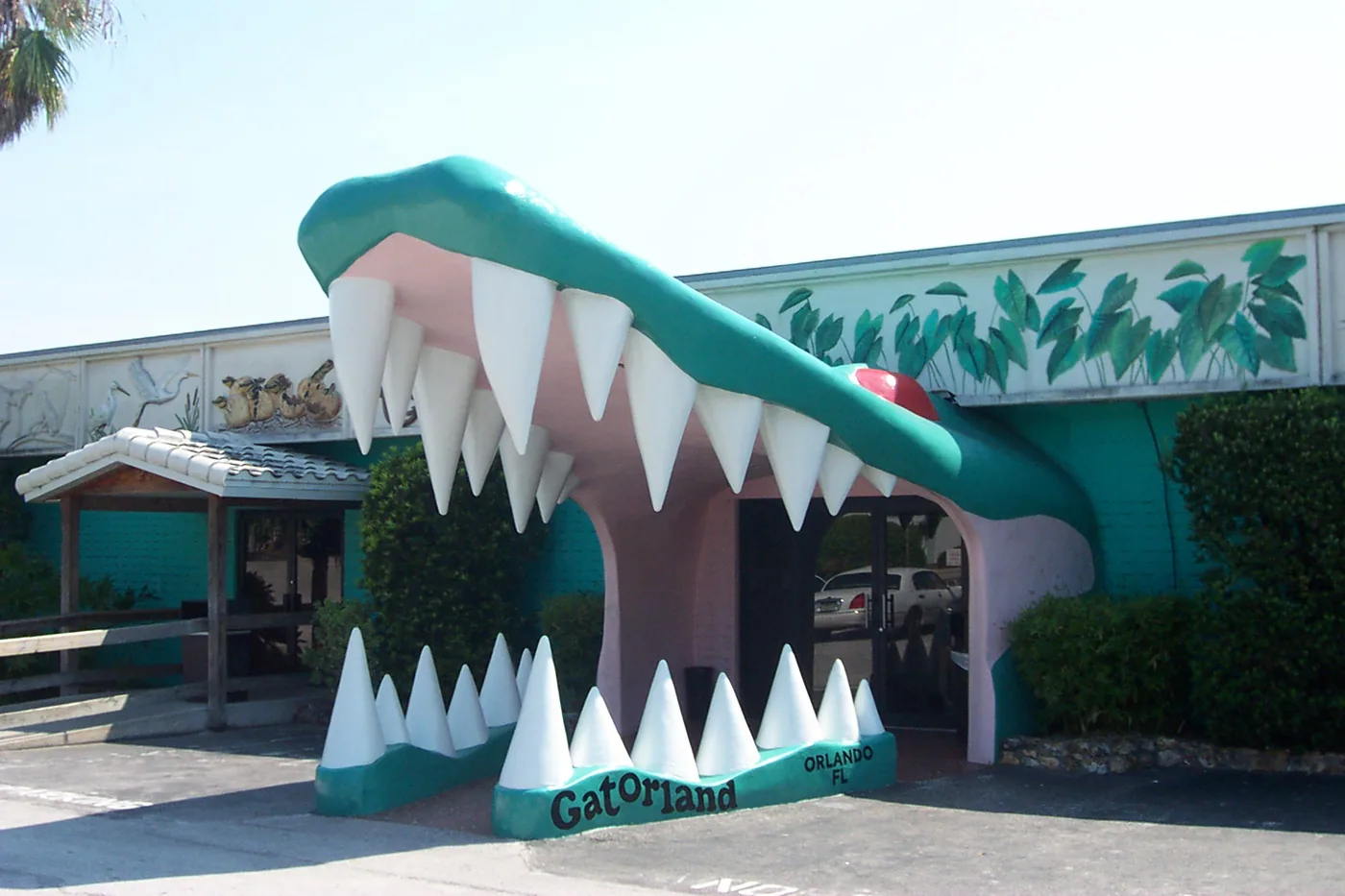 Gatorland's giant alligator-mouth entrance building in Orlando, teal and pink with rows of white teeth and 'Gatorland Orlando FL' lettered across the jaw