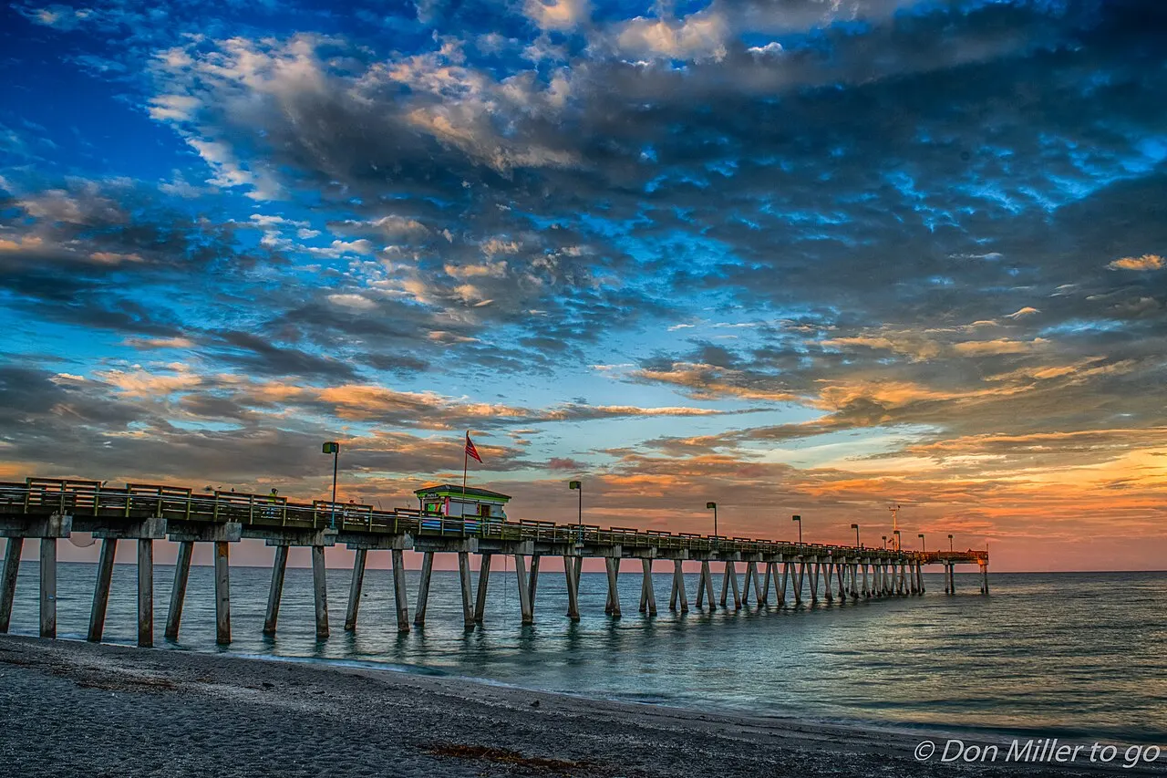 Sharky's Pier on the Venice Fishing Pier at sunset, a low building on pilings over the Gulf of Mexico with a flag flying and colorful sky behind it