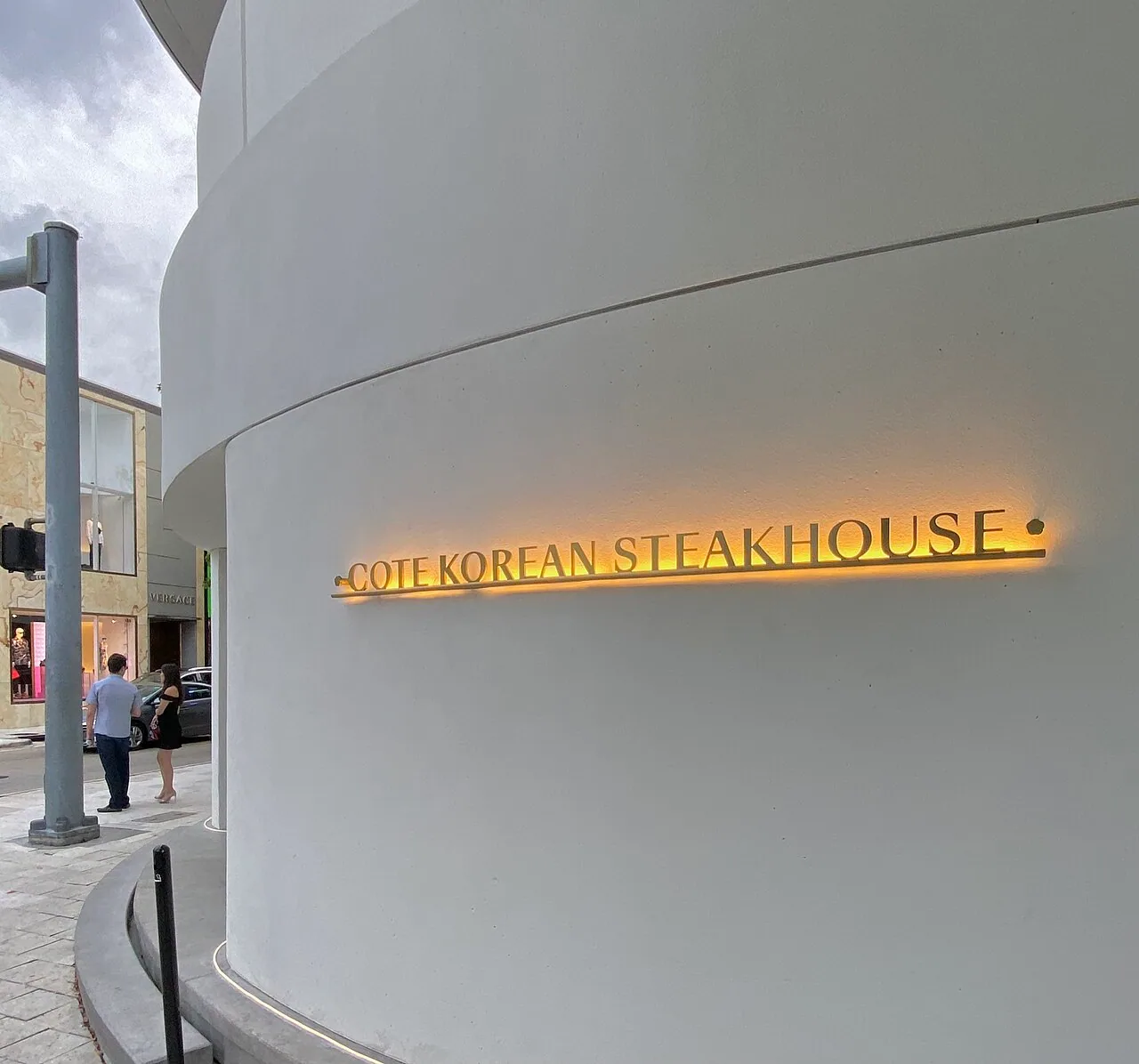 Backlit brass letters reading COTE KOREAN STEAKHOUSE mounted on the curved white facade of the restaurant's Design District building