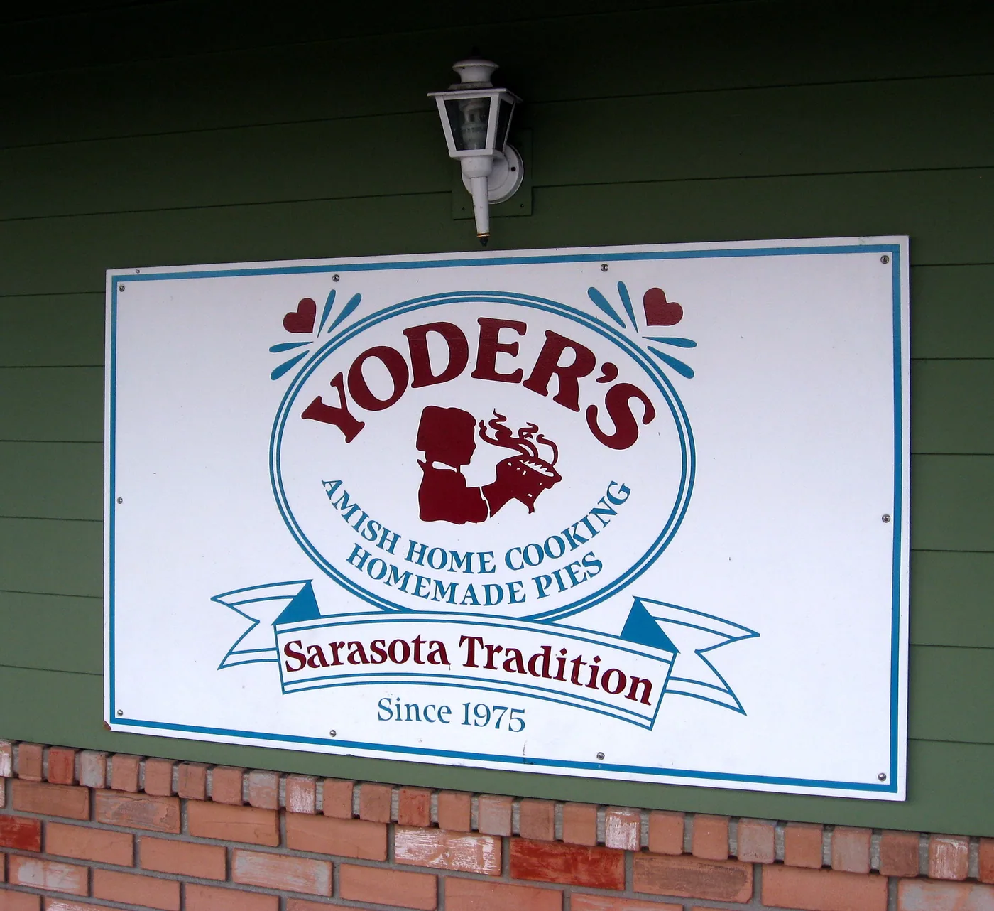 A sign mounted on Yoder's Restaurant's green exterior wall reading "Yoder's, Amish Home Cooking, Homemade Pies, Sarasota Tradition Since 1975"