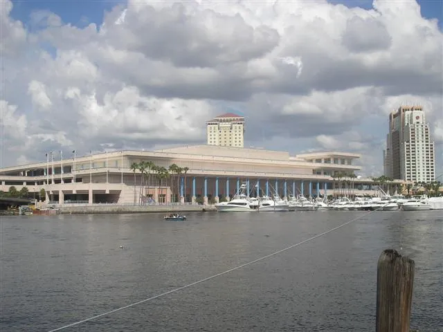 The Tampa Convention Center's low white building on the downtown waterfront, seen across the water with a hotel tower behind it