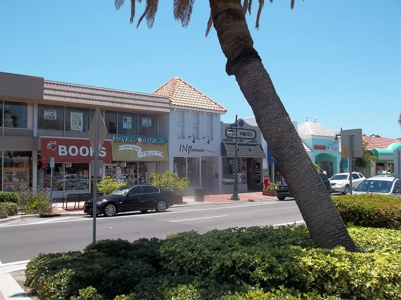 A row of shop storefronts on St. Armands Circle in Sarasota, including Circle Books and Loving Touches, under a Mediterranean-revival roofline with a palm tree in the foreground