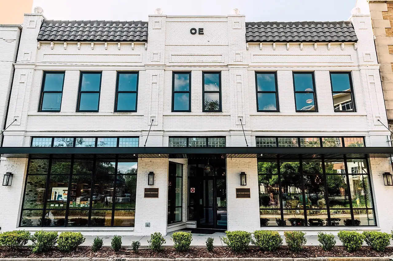 The white two-story facade of Oxford Exchange in Tampa, with a bold 'OE' monogram above the entrance and glass storefront windows below