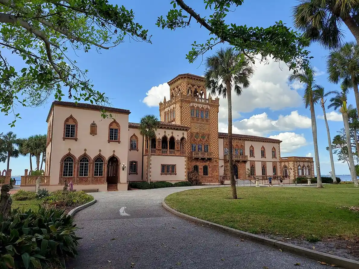 Ca' d'Zan, the Ringlings' Venetian Gothic mansion on Sarasota Bay, showing its tower and bayfront wings from the lawn, with palm trees in the foreground