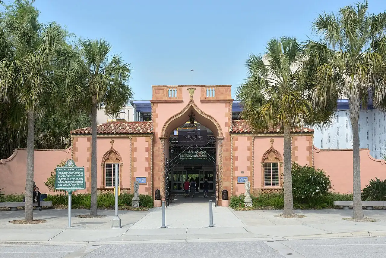 The pink Venetian Gothic entrance arch of The Ringling museum in Sarasota, with a "Welcome to The Ringling" sign under the arch and palm trees framing the gate