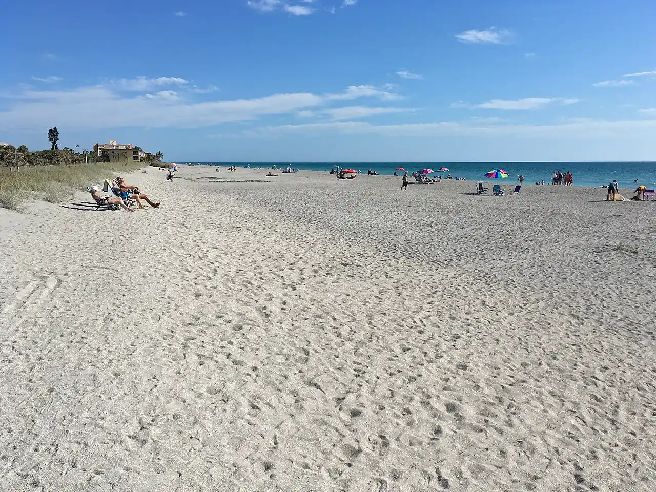 Coarse sand beach at Turtle Beach on Siesta Key, with a few beachgoers, umbrellas and low-rise buildings along the shoreline in the distance