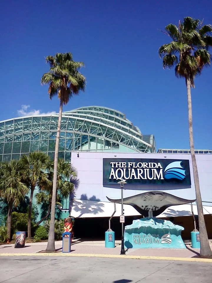 The Florida Aquarium's glass-domed entrance building with its blue wordmark sign, palm trees and a manta ray sculpture out front