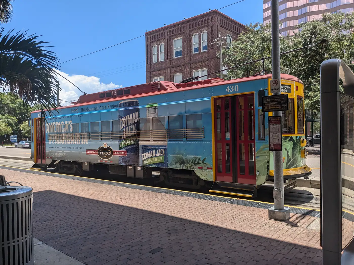 TECO Line Streetcar No. 430, painted blue and yellow, stopped on downtown Tampa tracks with the city skyline behind it