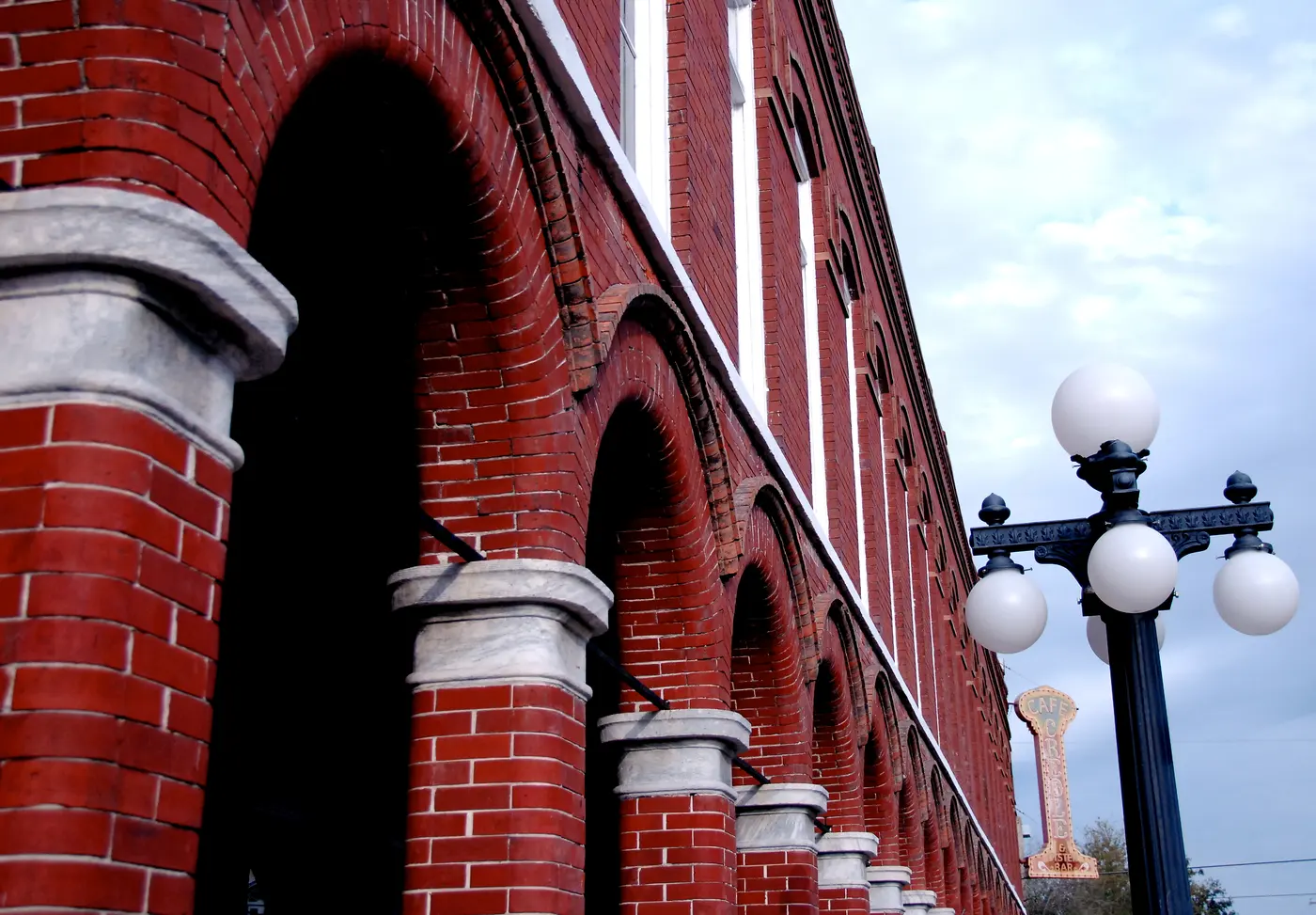 A row of red-brick arched arcades on a historic Ybor City cigar-factory building, with a Victorian street lamp in front