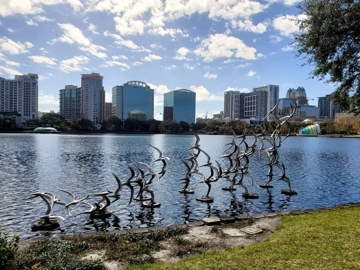 Stainless-steel bird sculptures rising from Lake Eola with the downtown Orlando skyline behind