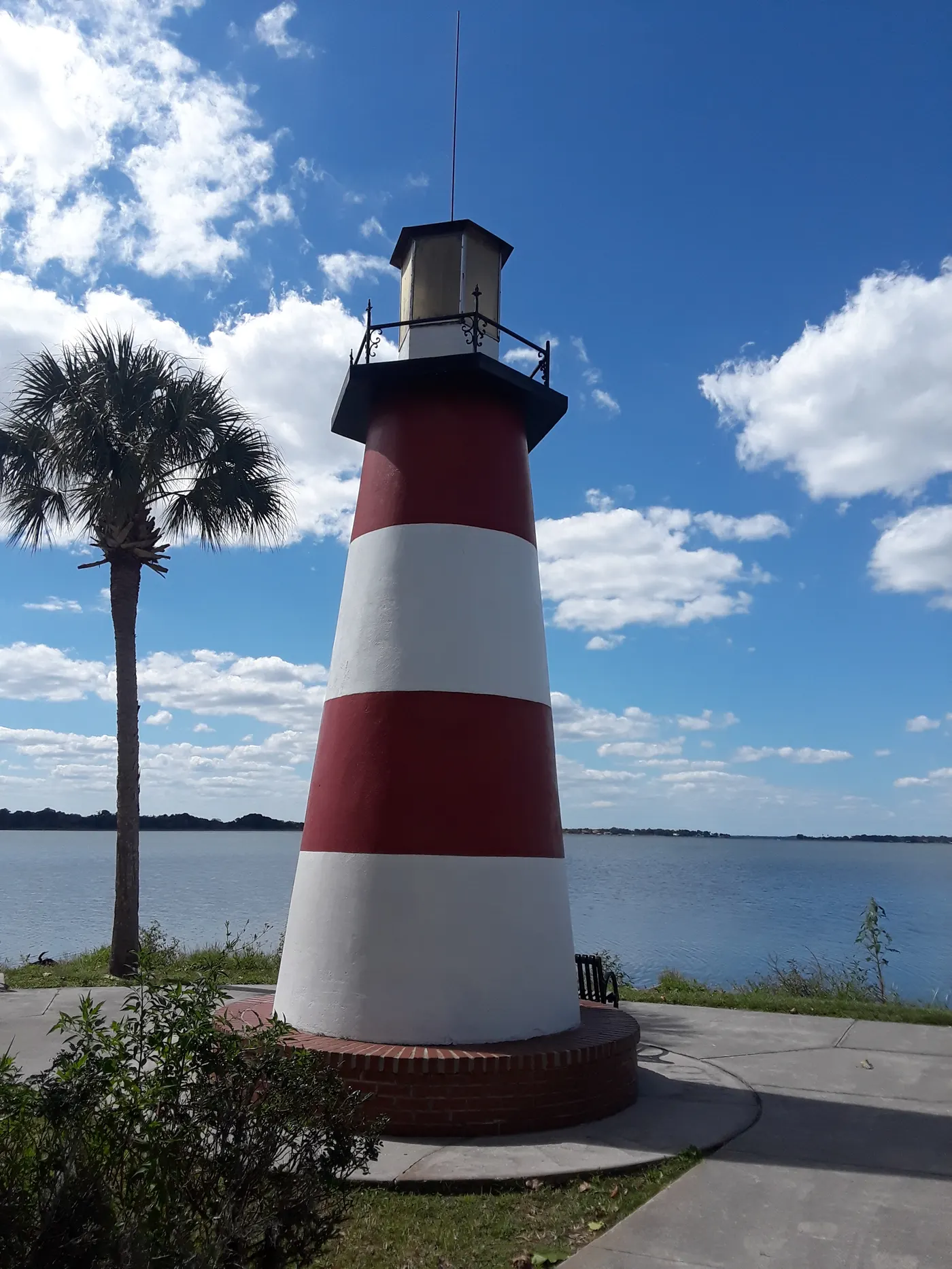 The red-and-white Mount Dora Lighthouse on the shore of Lake Dora, with a palm tree beside it