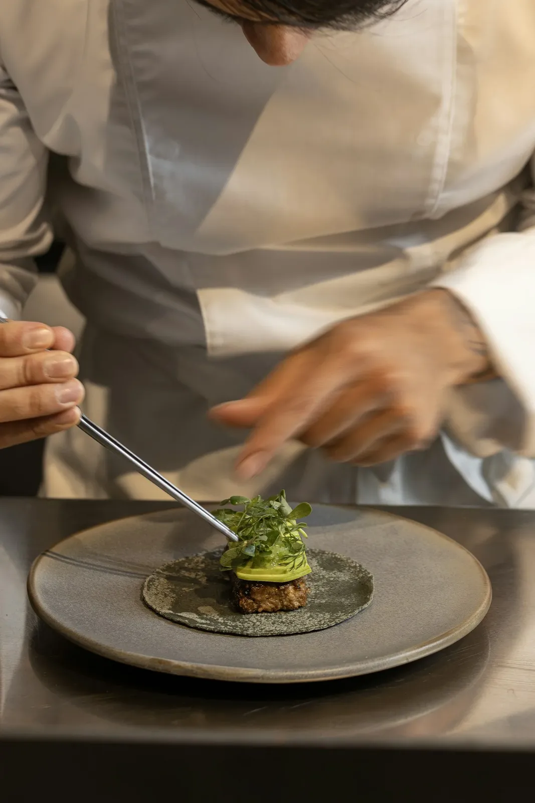 Chef using tweezers to finish a plated restaurant dish